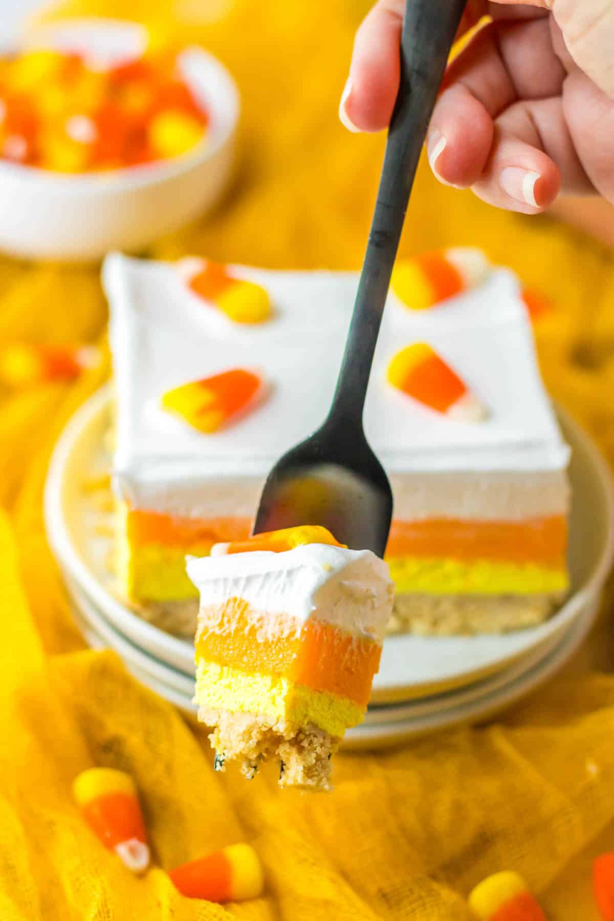 A person holding a piece of candy corn layered cake.