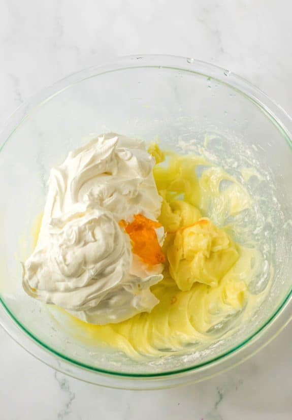 Whipped cream and yellow mixture in a glass bowl.