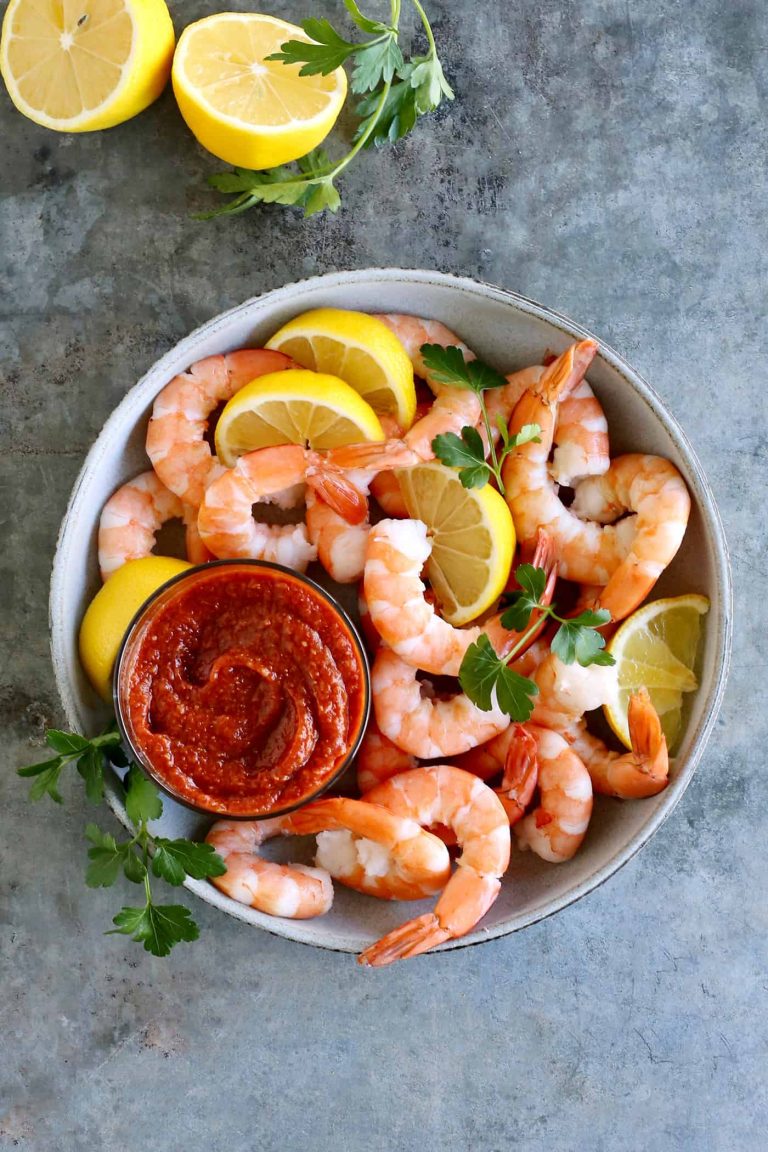 Shrimp in a bowl with sauce and lemons.