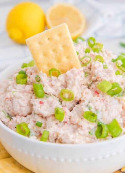 A bowl of tuna salad with crackers and lemons.