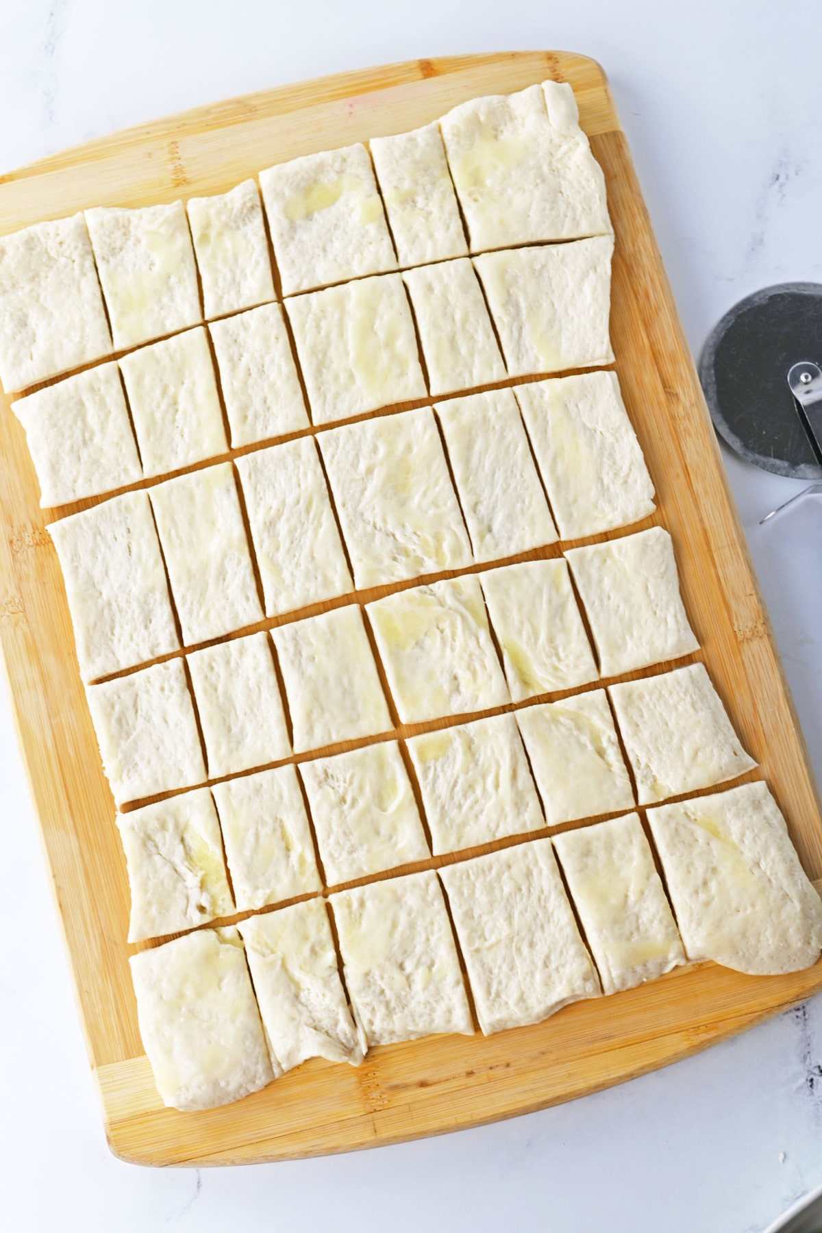 A wooden cutting board with dough squares in it for Pigs in a Blanket recipe