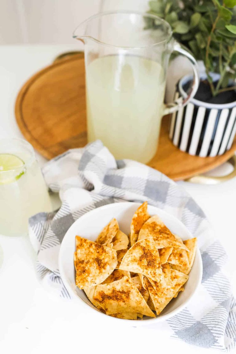 A bowl of nachos next to a pitcher of lime juice.