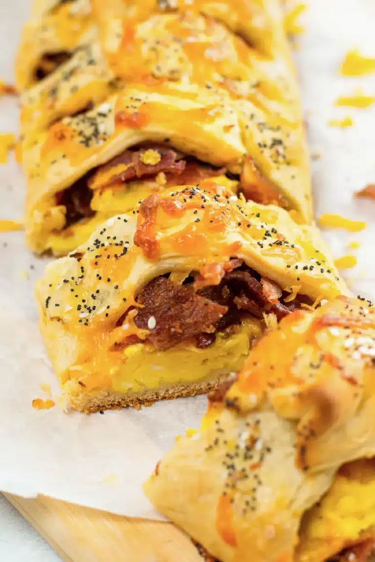 A breakfast pastry with eggs and bacon on a cutting board.