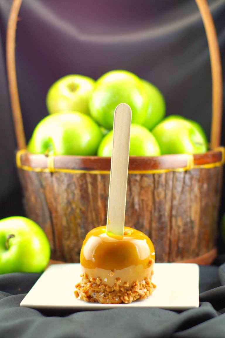 A basket of apples on a table with a caramel apple on a stick.