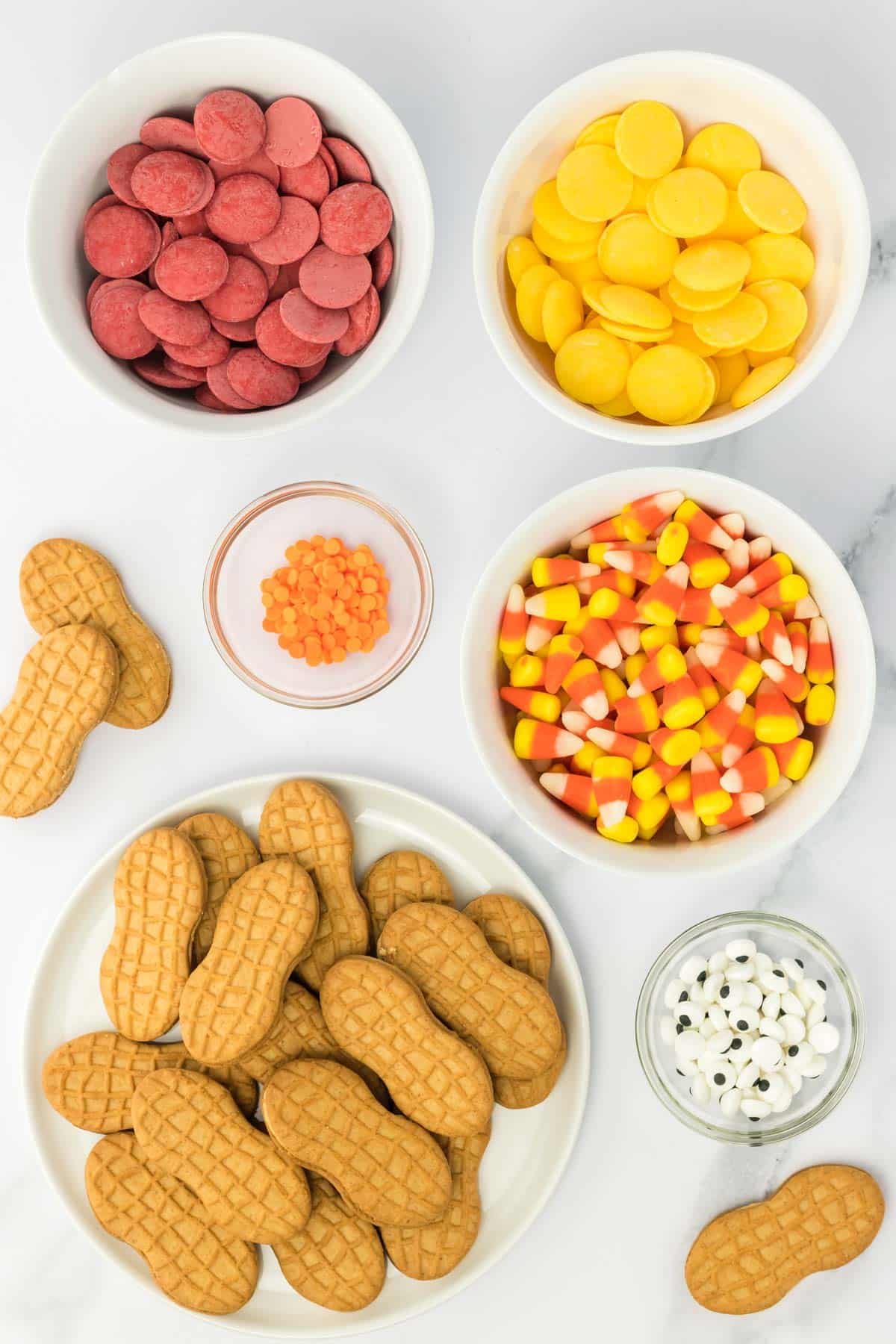 A variety of candy and Nutter Butter cookies in bowls on a white surface.