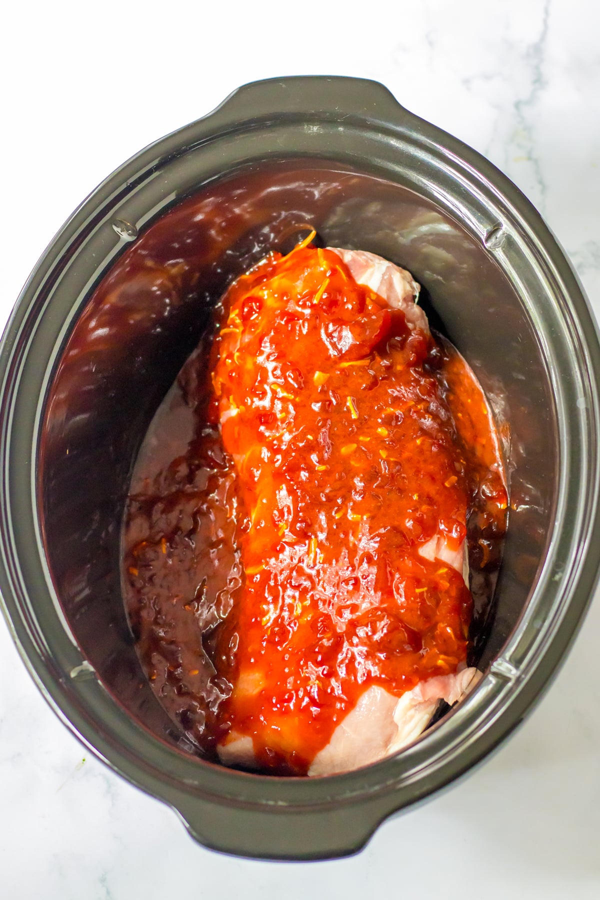 Adding cranberry sauce over pork in a slow cooker.