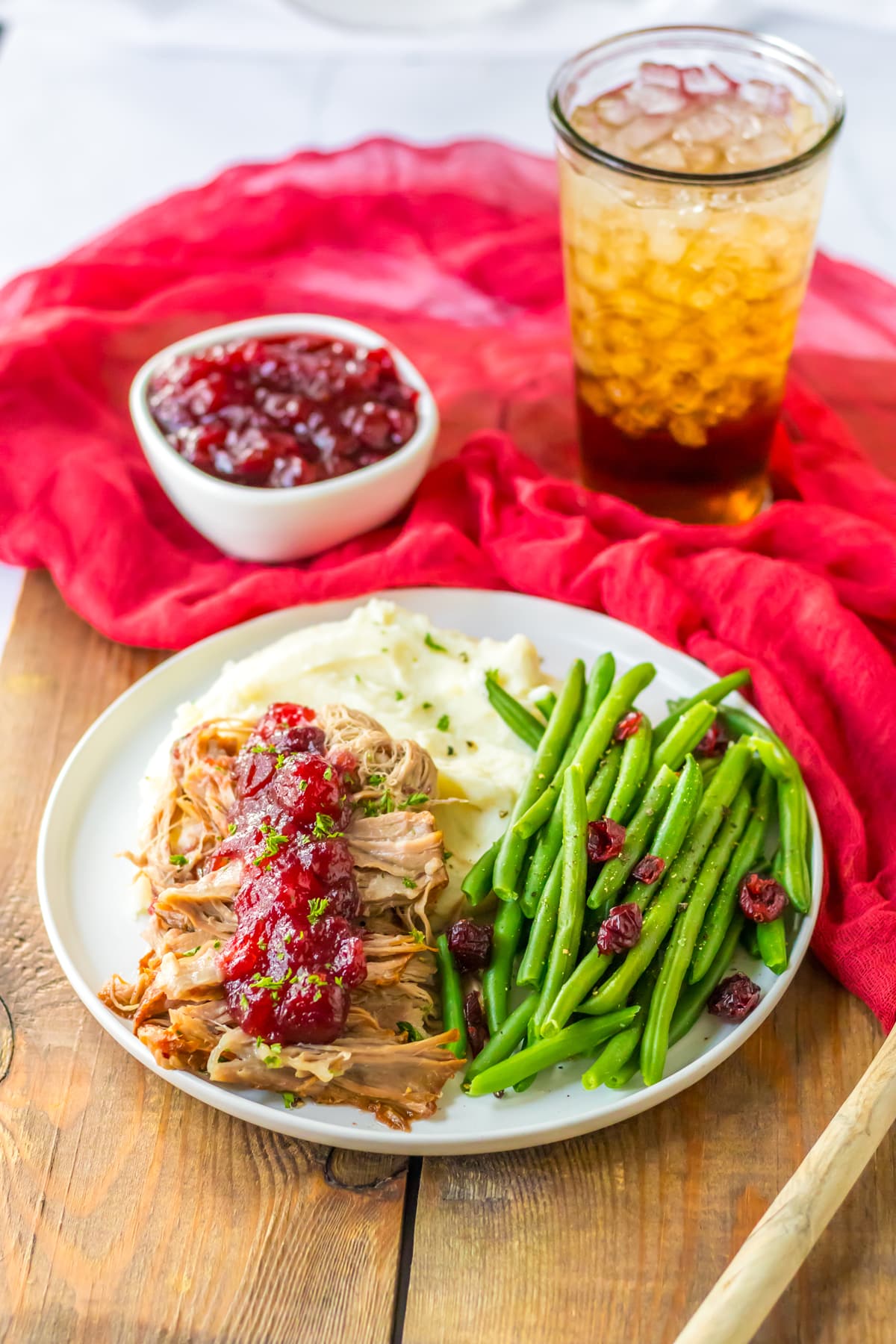 A plate of Slow Cooker Cranberry Pork with beans, drink and a sauce.