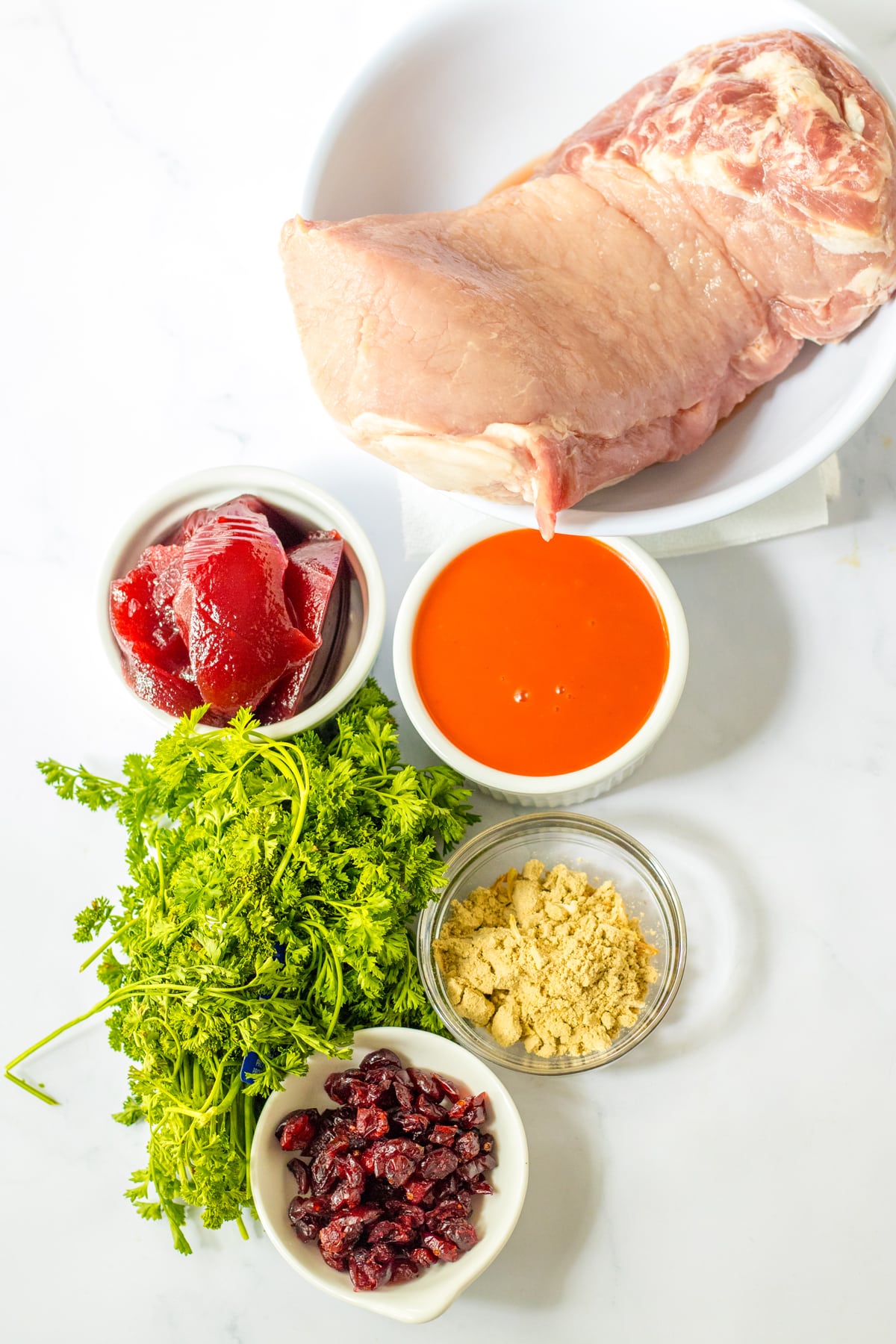 Ingredients for Slow Cooker Cranberry Pork include pork loin roast, dry onion soup mix, french dressing, canned cranberry sauce (jellied or whole cranberry sauce), and dried cranberries and parsley for garnish