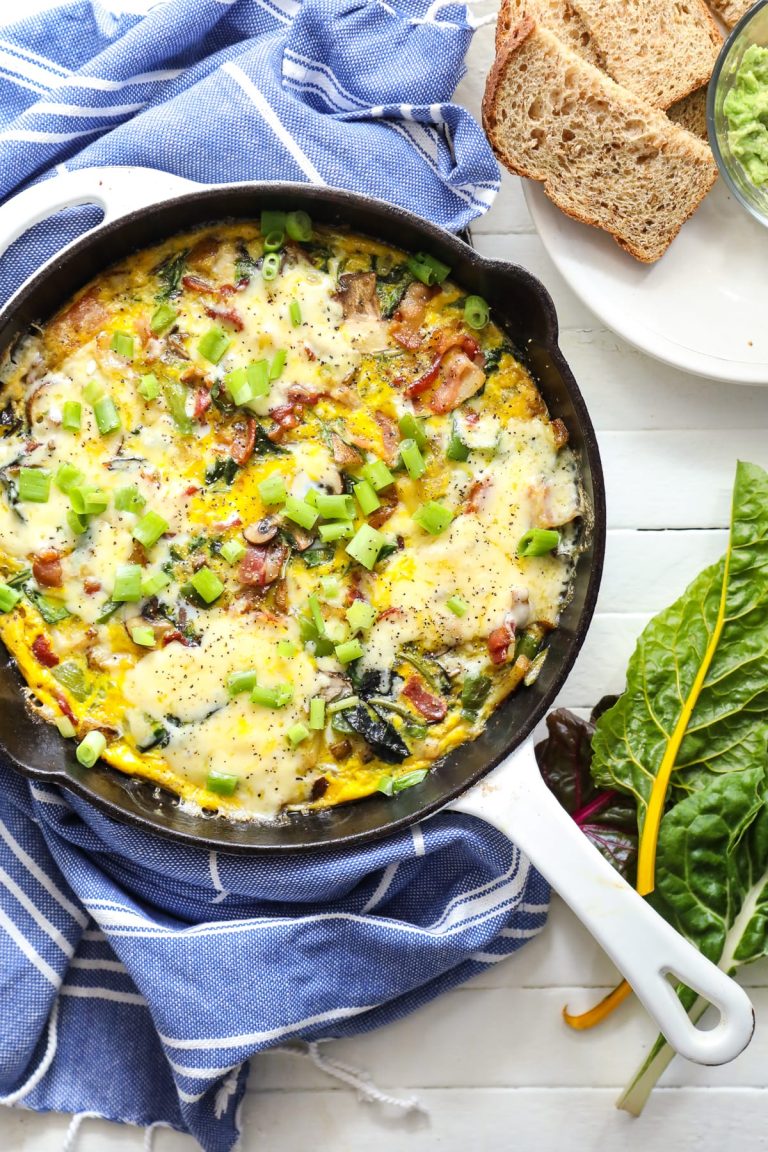 An omelet with spinach and bacon in a skillet.