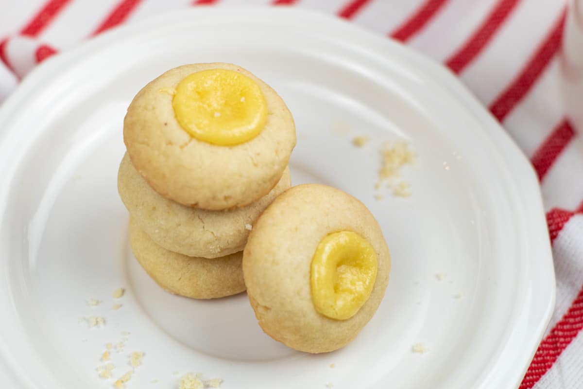 A stack of lemon cookies on a white plate with a cup of coffee.