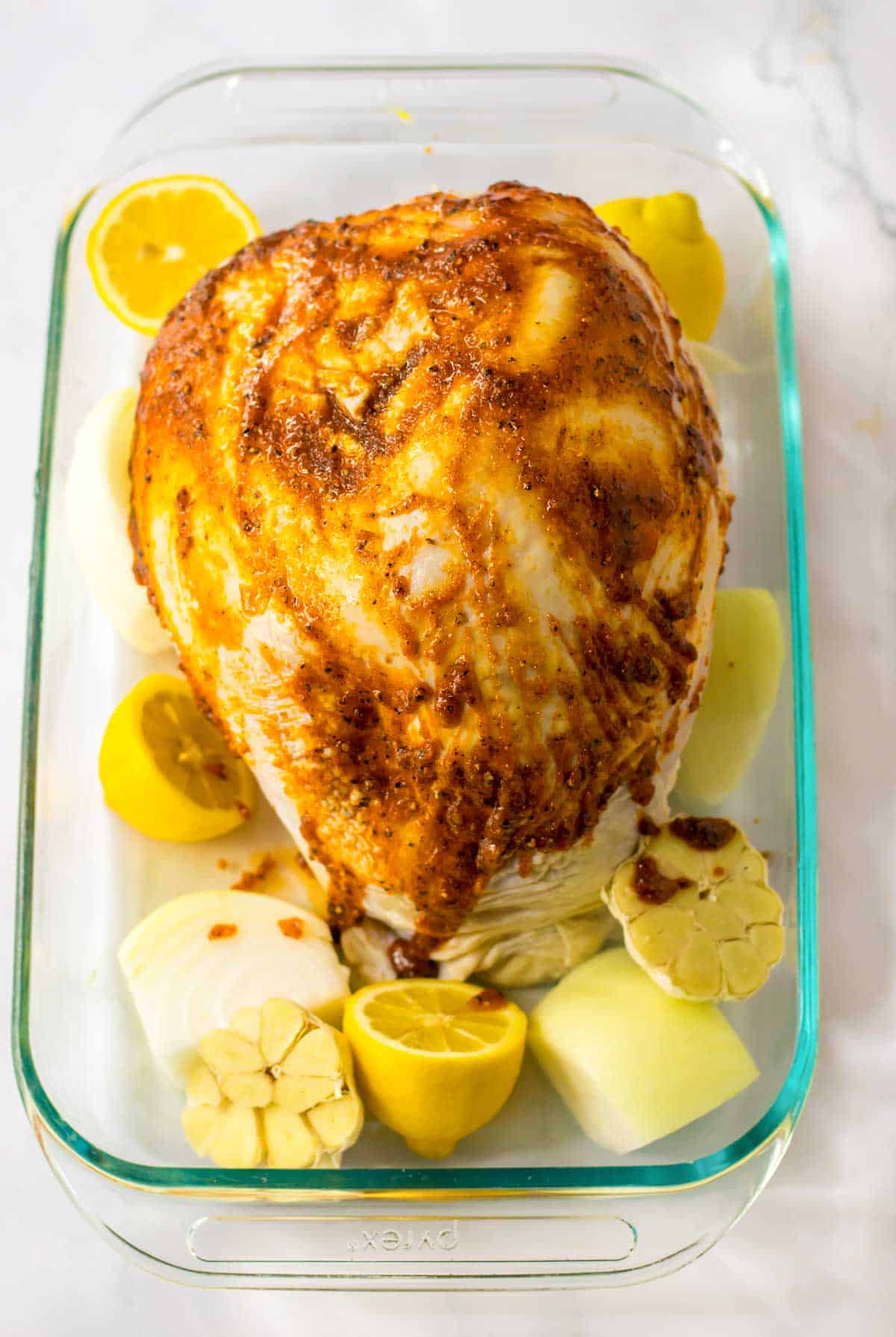 A roasted turkey breast in a glass baking dish with lemons and onions.