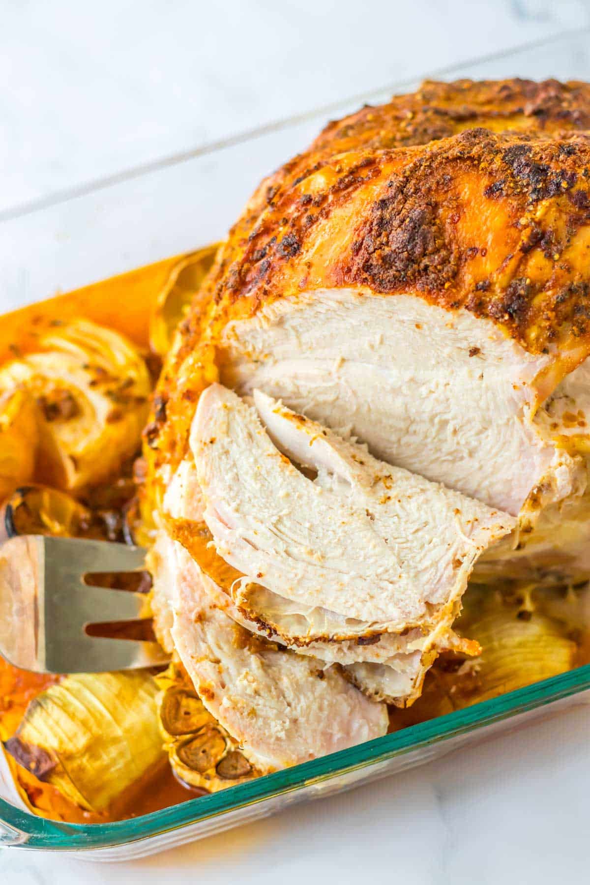 A roasted turkey with artichokes in a glass baking dish.