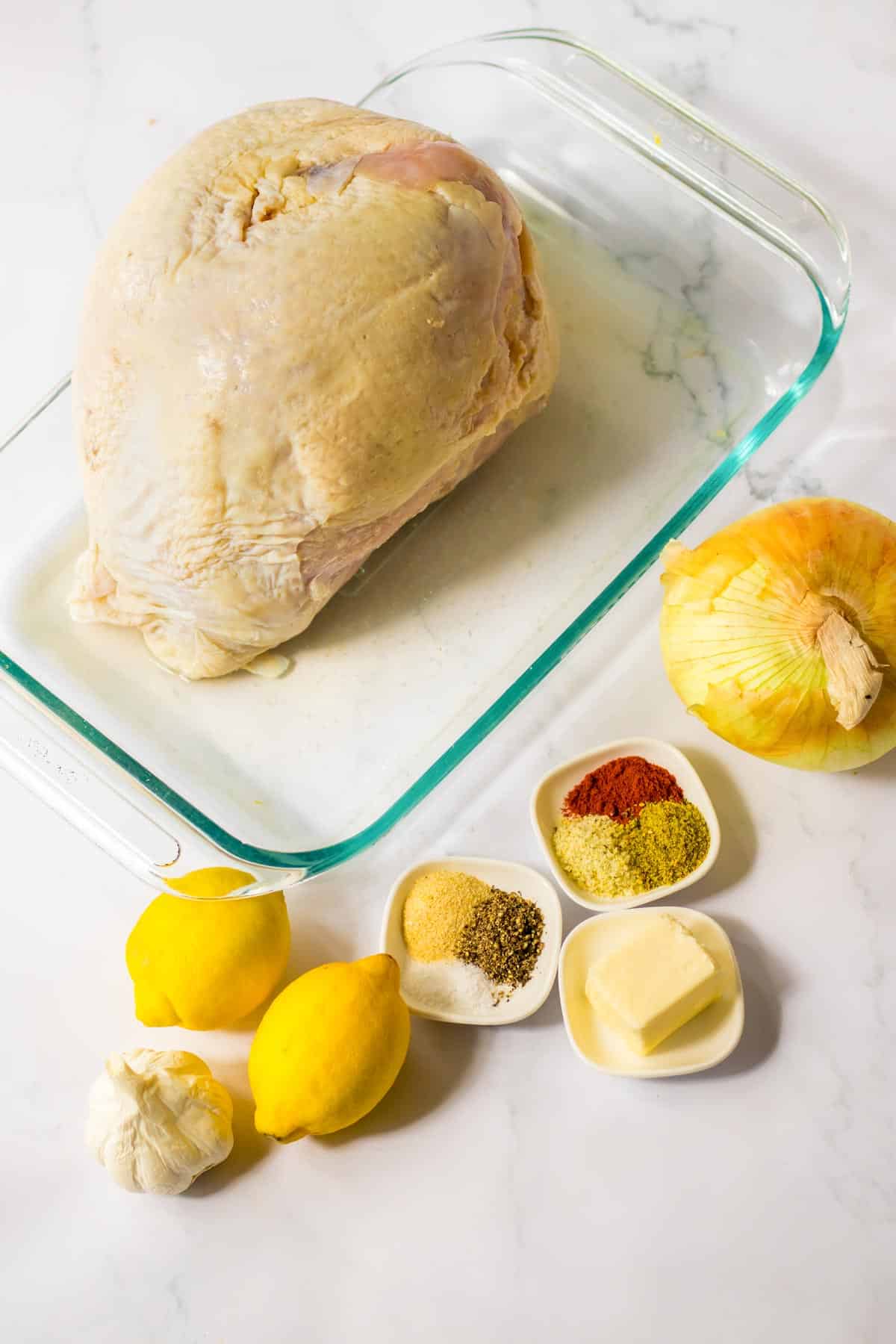 A glass dish with a roasted chicken, lemons, and other ingredients.