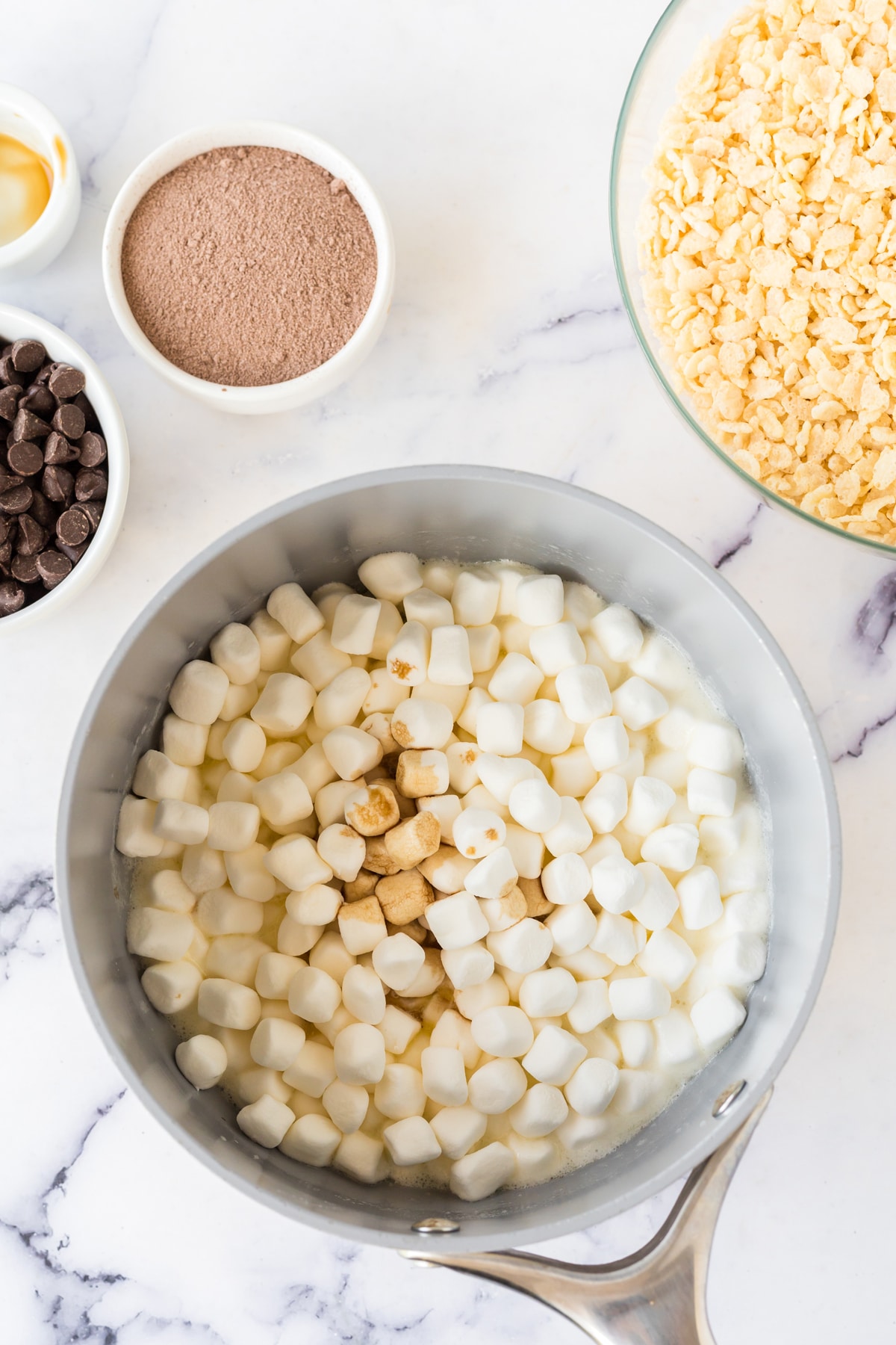 Melting marshmallows in a pan is one process of preparing Hot Chocolate Rice Krispy Treats