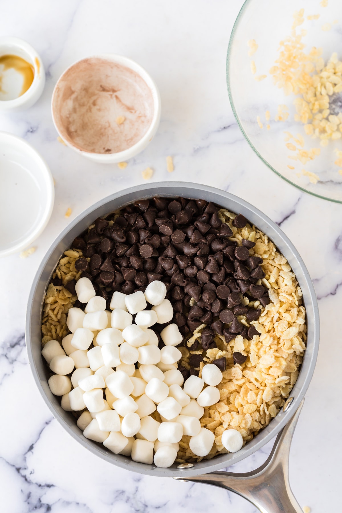 A pan with marshmallows, chocolate chips, rice krispies cereal, and other ingredients combined to make Hot Chocolate Rice Krispy Treats