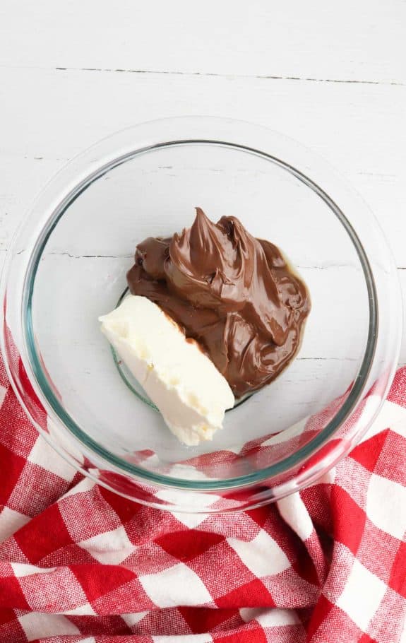 nutella and cream cheese in a glass bowl on a red and white checkered tablecloth.
