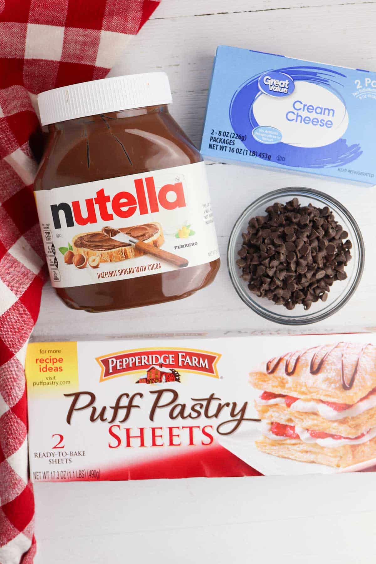 Nutella puff pastry sheets and chocolate chips on a checkered table.