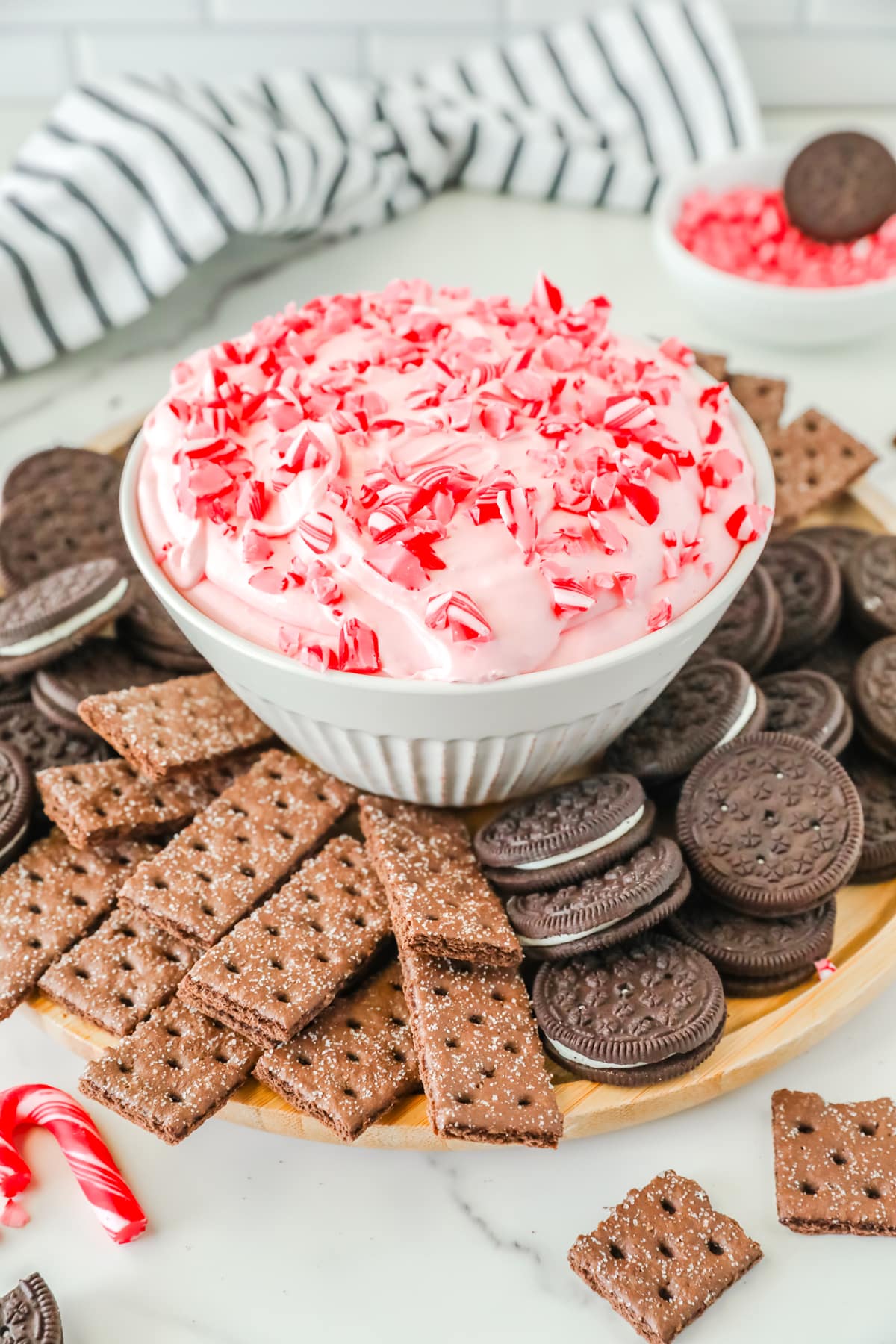 Peppermint Fluff with oreos, graham crackers and candy canes on a wooden plate.