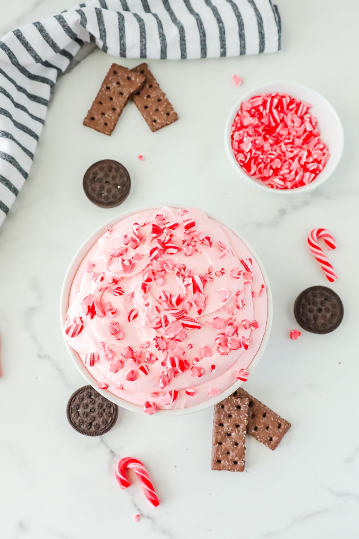 A bowl of Peppermint Fluff with candy cane, oreos and sprinkles.