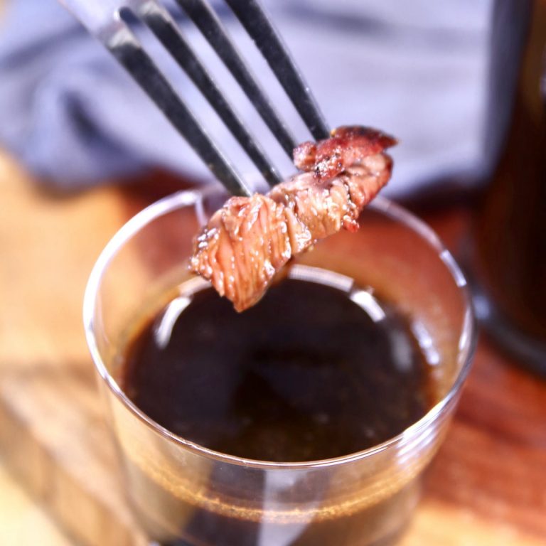 A fork is holding a piece of steak in a glass.