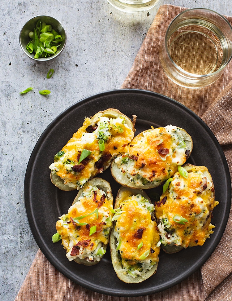 Cheesy stuffed potatoes on a plate with a glass of wine.