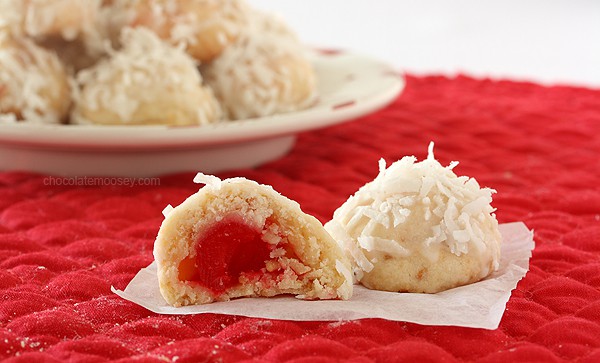 A plate of coconut cookies with a cherry in the middle.