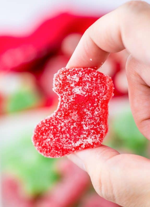 A person holding a red gummy Christmas gumdrop in their hand.