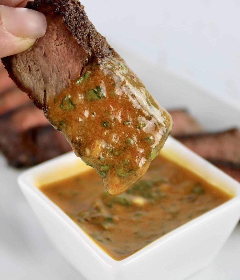 A person dipping a steak into a bowl of sauce.