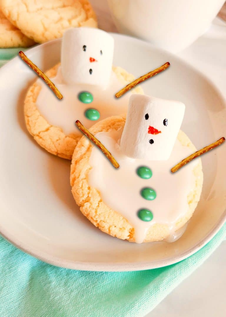 Two snowman cookies on a plate with marshmallow sticks.