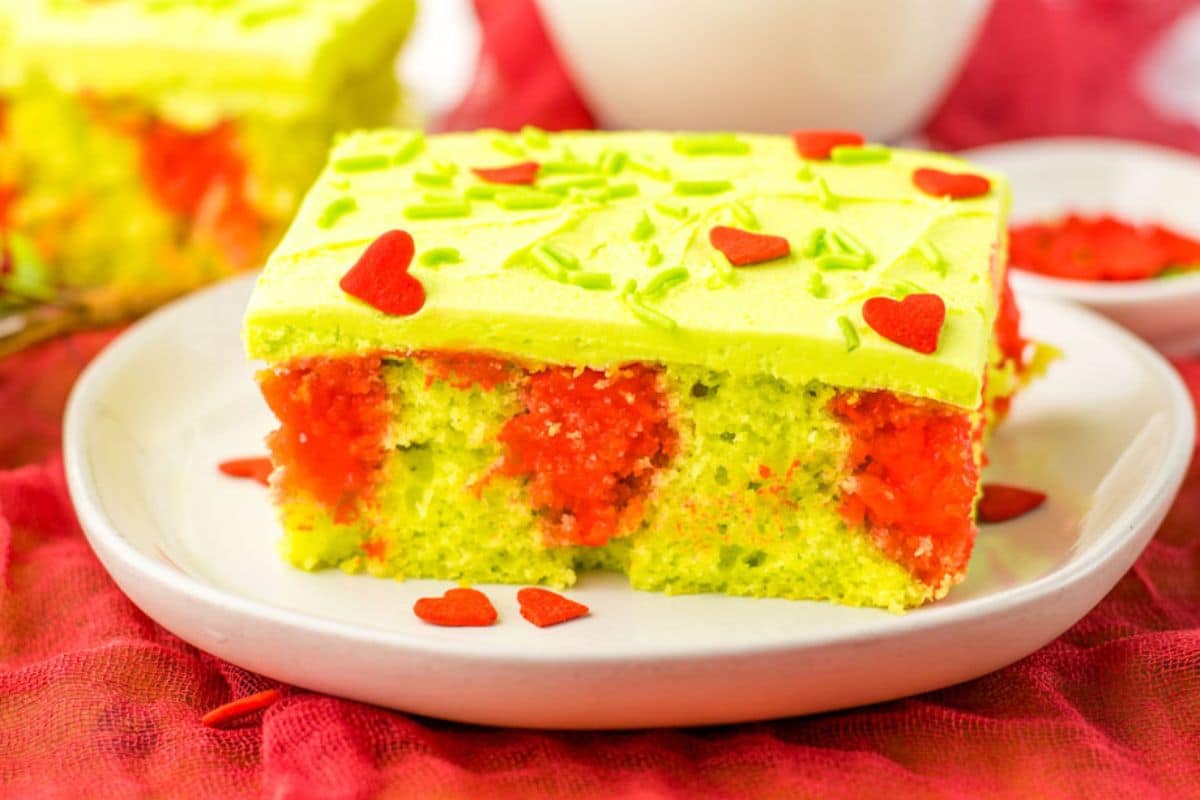 A Grinch poke cake with green frosting and red hearts on a plate.