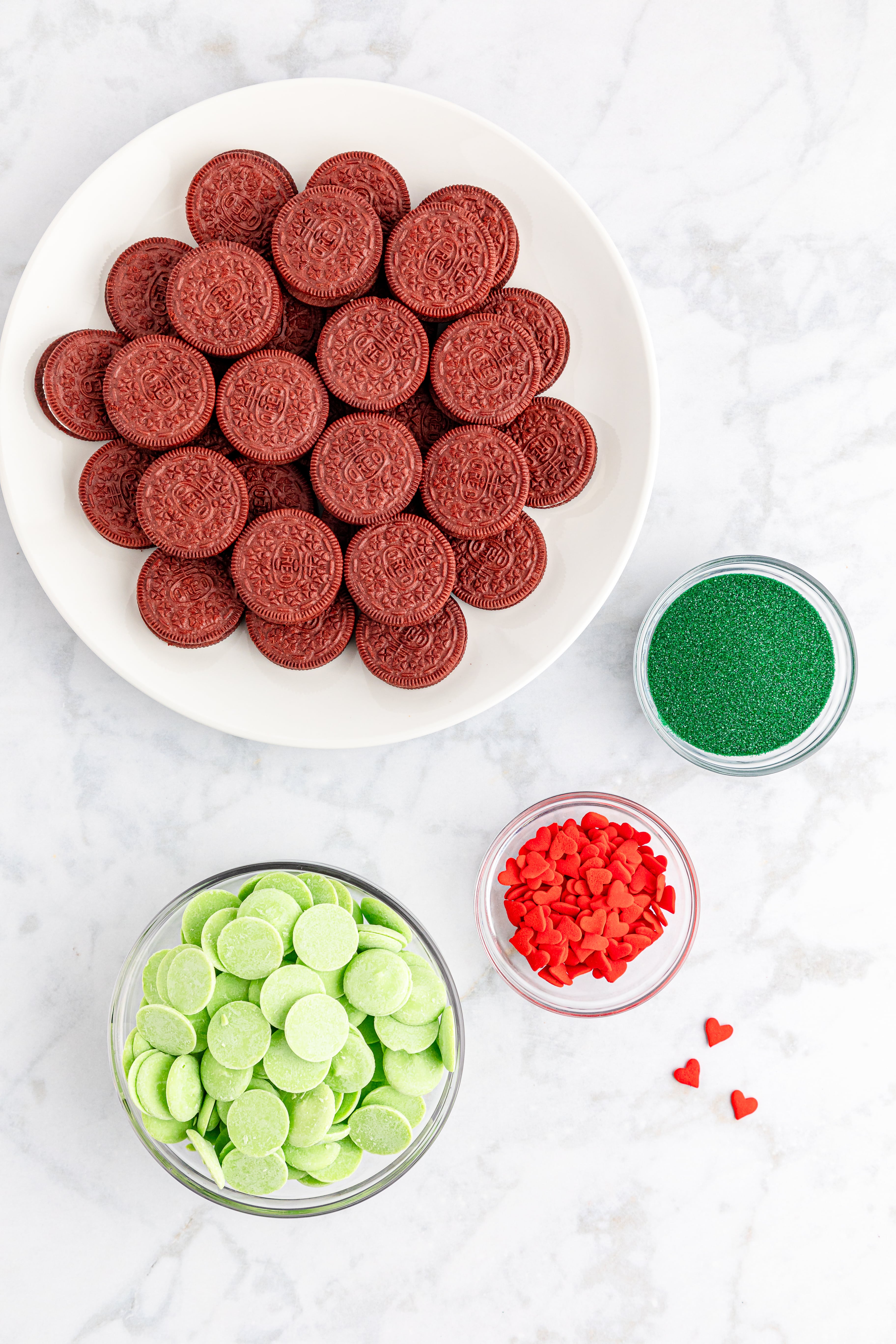 Red velvet Oreos, green sprinkles, red candy hearts and light green candy melts on marble counter