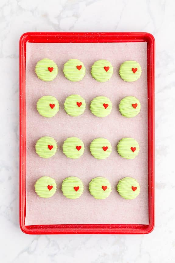 light green Grinch red velvet Oreos with candy heart on red baking tray