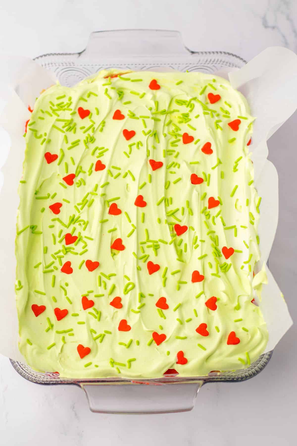 A Grinch-themed layered dessert featuring a green and red heart shaped cake.