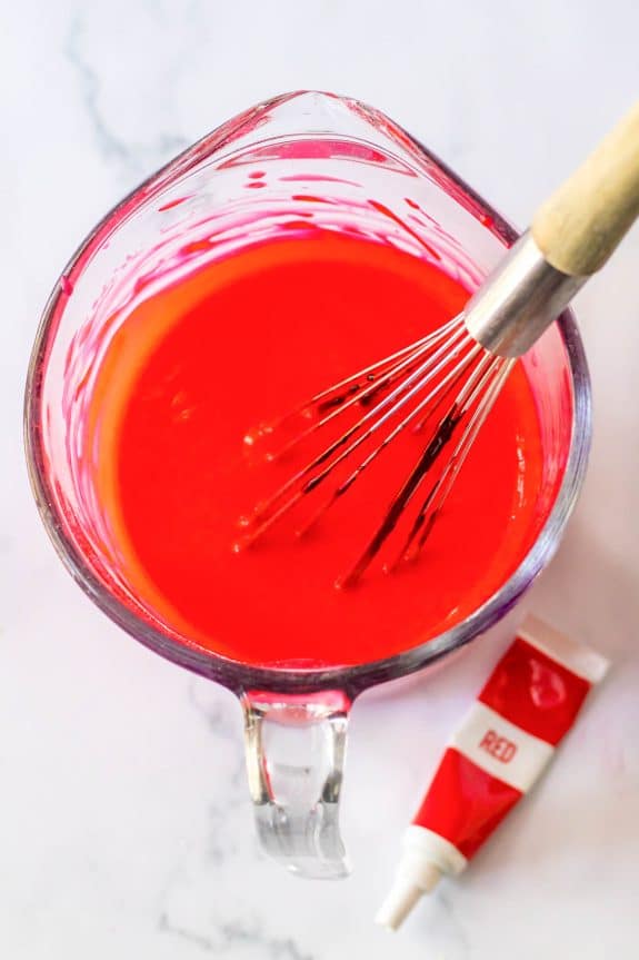 A bowl of red icing with a whisk in it.