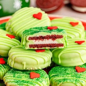 Oreo cookies with green frosting and hearts on a plate, inspired by the Grinch.