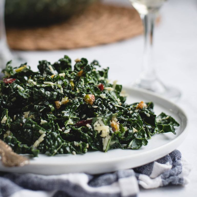 Kale salad on a white plate with a glass of wine.