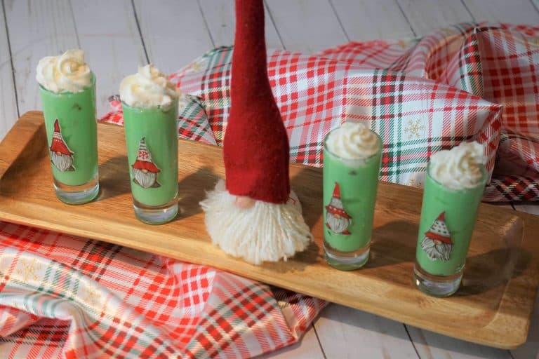 Green gnome shot glasses with whipped cream and a santa hat.