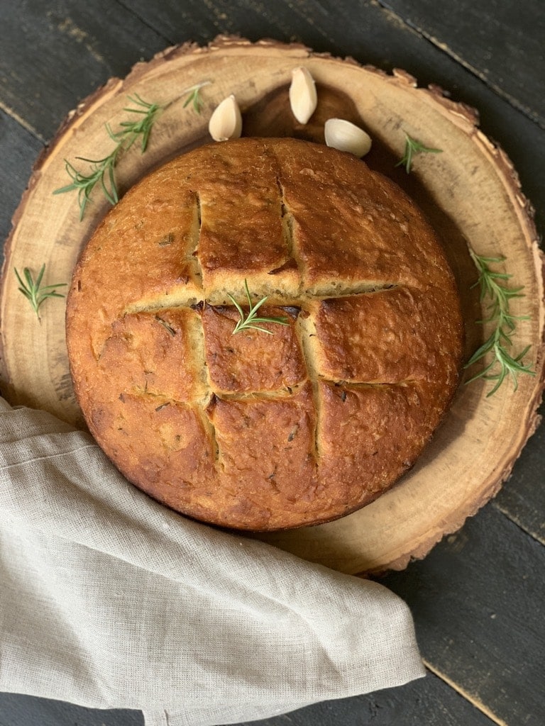 A loaf of bread with rosemary on a wooden plate.