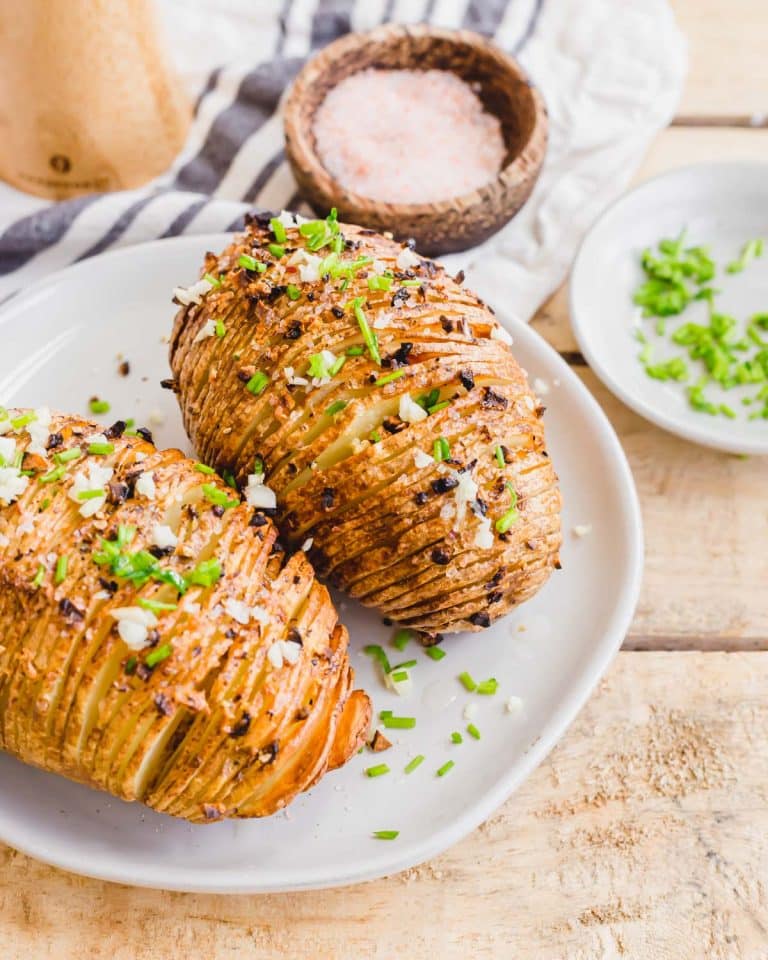 Two roasted potatoes on a plate with salt and chives.
