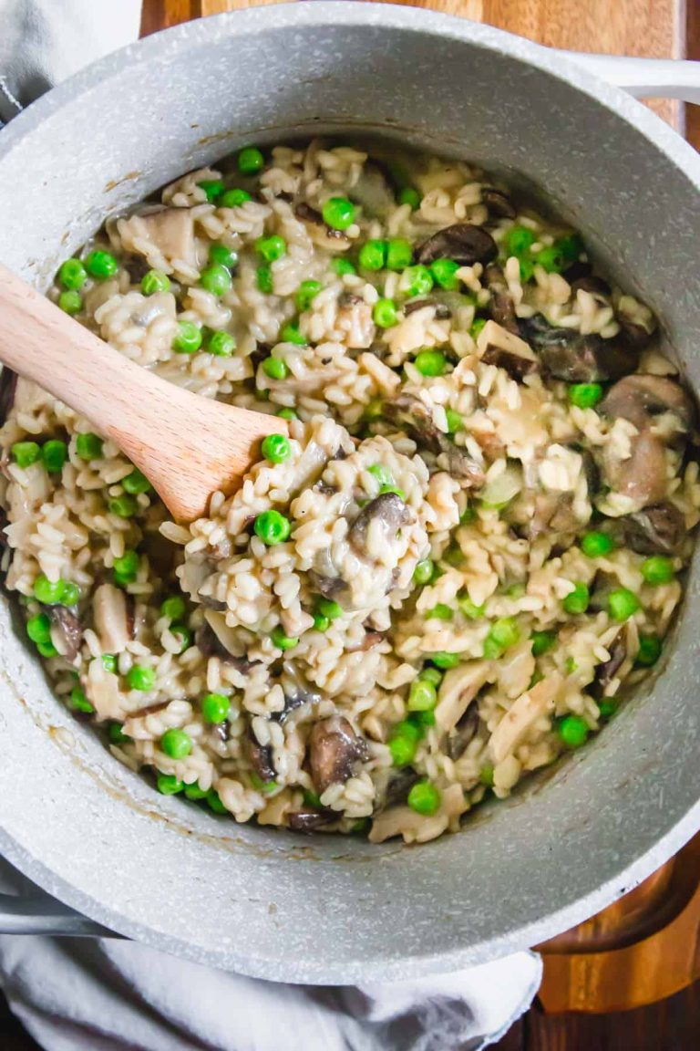 Mushroom and pea risotto in a pan with a wooden spoon.
