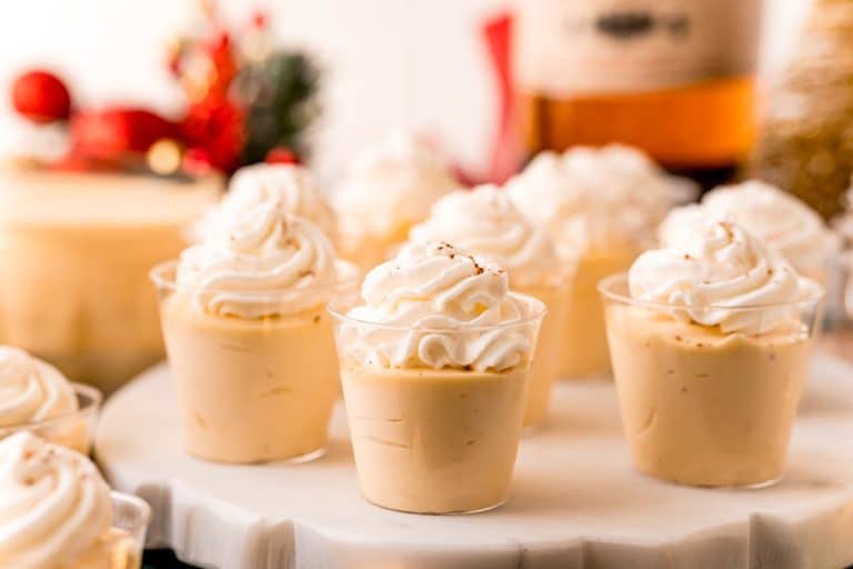 A group of cups with whipped cream and a bottle of whiskey.
