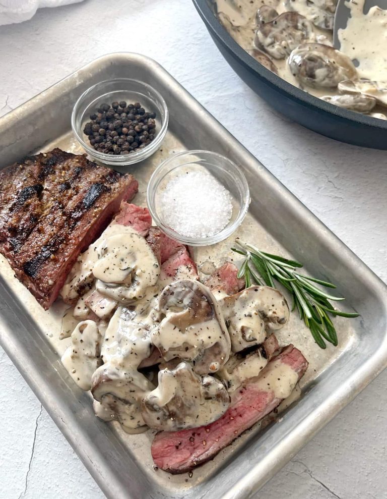 A pan with steak, mushrooms and sauce on it.