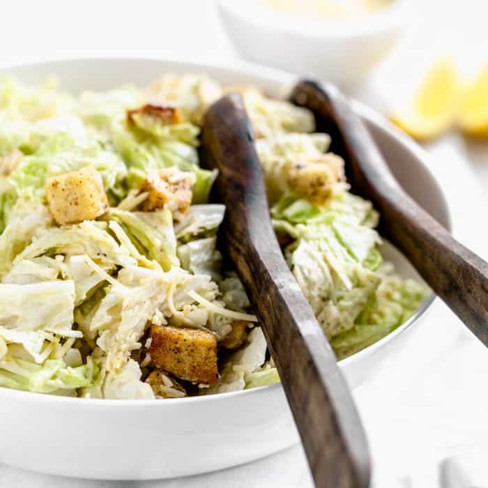 A bowl of caesar salad with croutons and lemon.