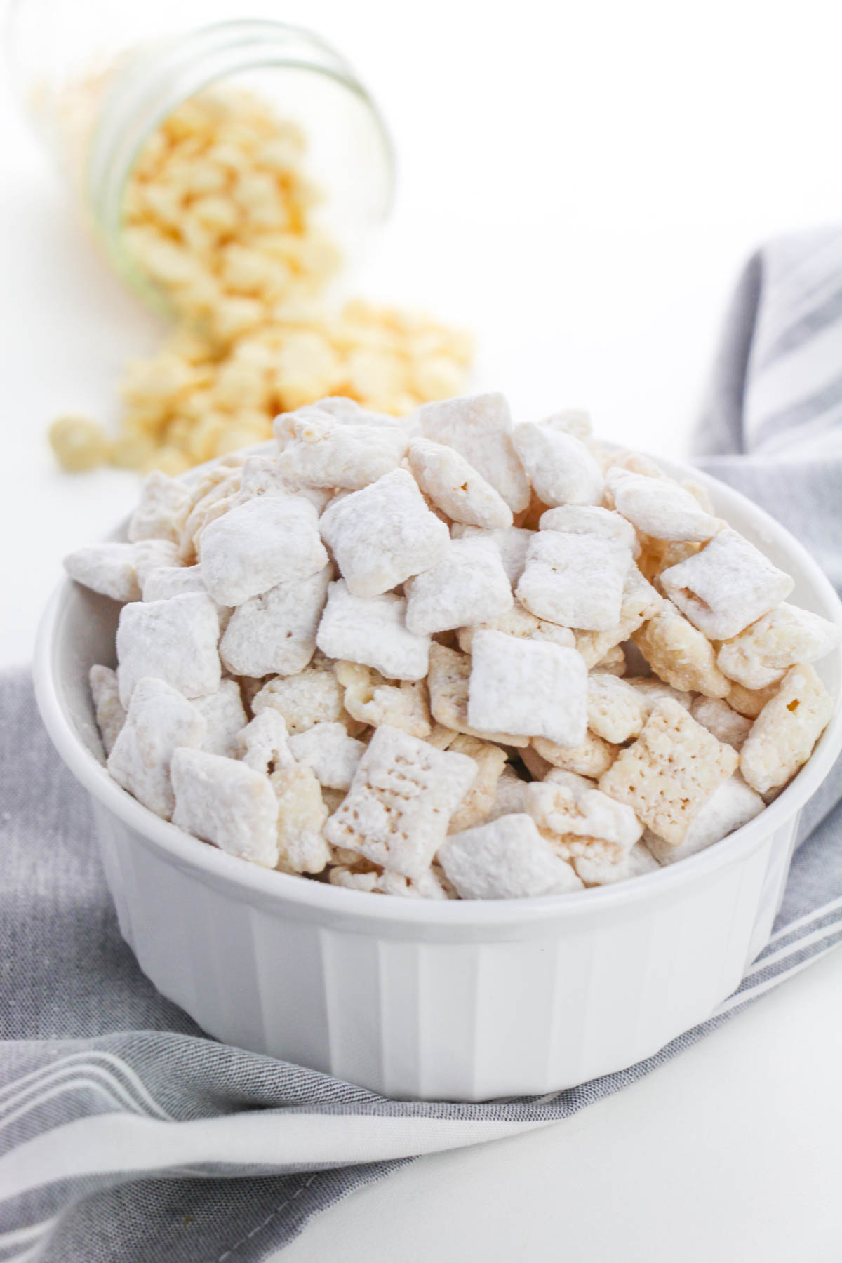 A white bowl of white chocolate puppy chow in front of a napkin.