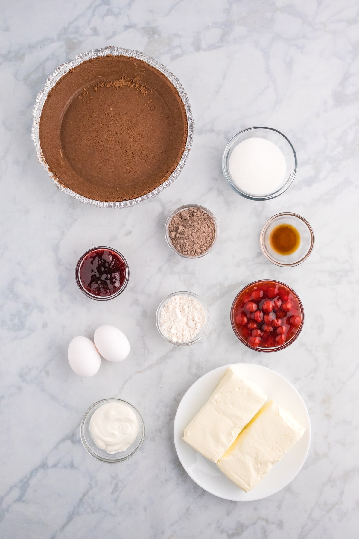 Ingredients for Chocolate Cherry Cheesecake are premade chocolate pie crust, softened cream cheese, granulated sugar, large eggs, sour cream, all purpose flour, vanilla extract, instant chocolate pudding mix, cherry preserves, cherry pie filling, and whipped cream for topping.