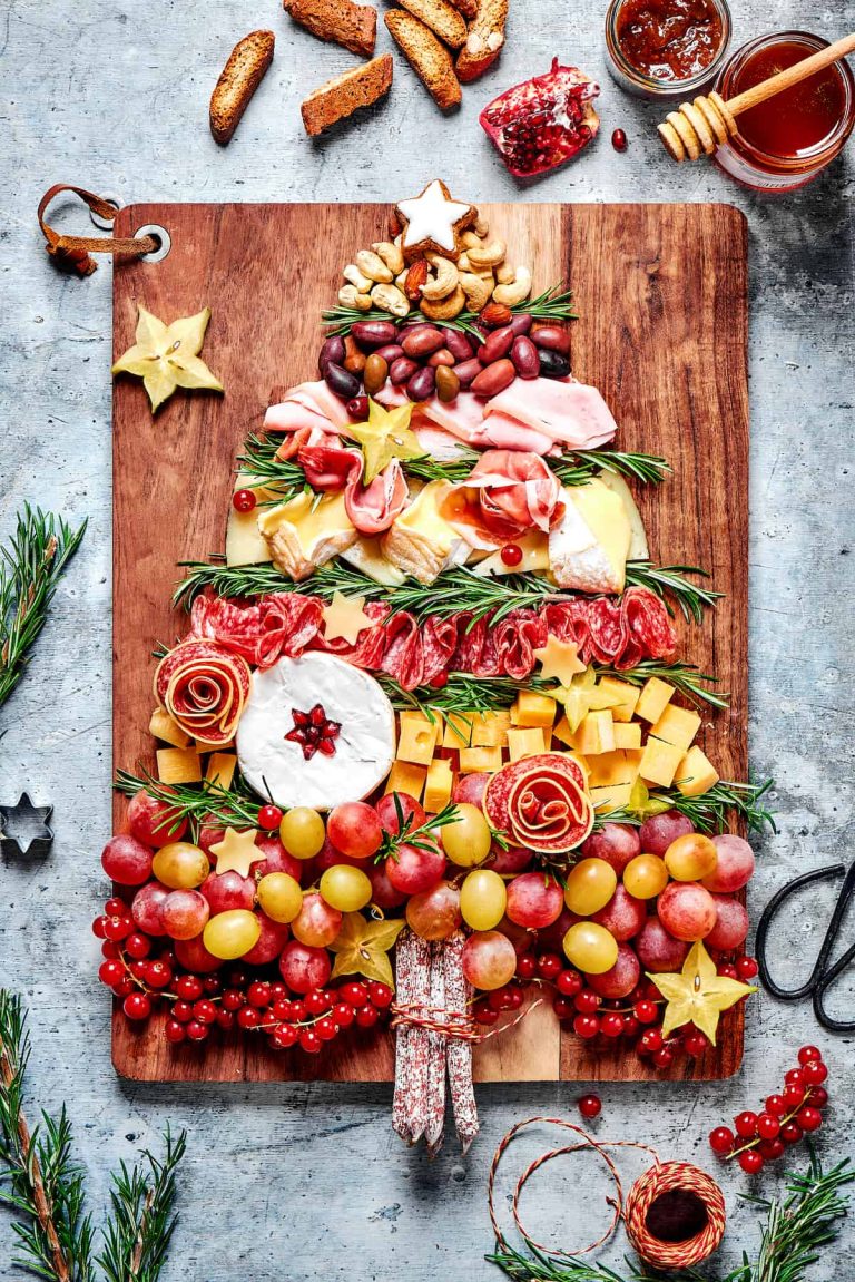 A christmas tree made of cheese, fruits and nuts on a wooden cutting board.
