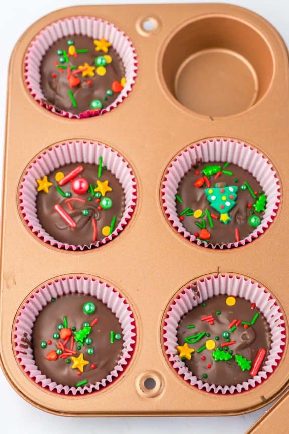 Chocolate peanut butter cups in a muffin tin with sprinkles.