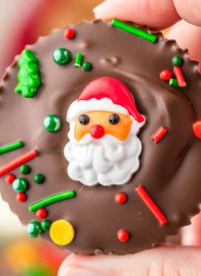 A person holding up a chocolate covered santa claus cookie.