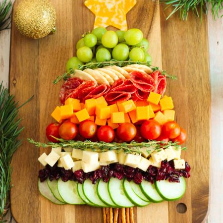 A christmas tree made of fruits and vegetables on a wooden cutting board.