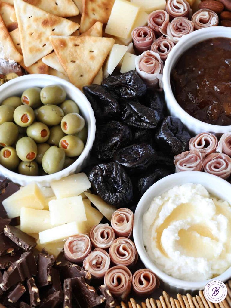 A wicker basket filled with olives, crackers and dips.